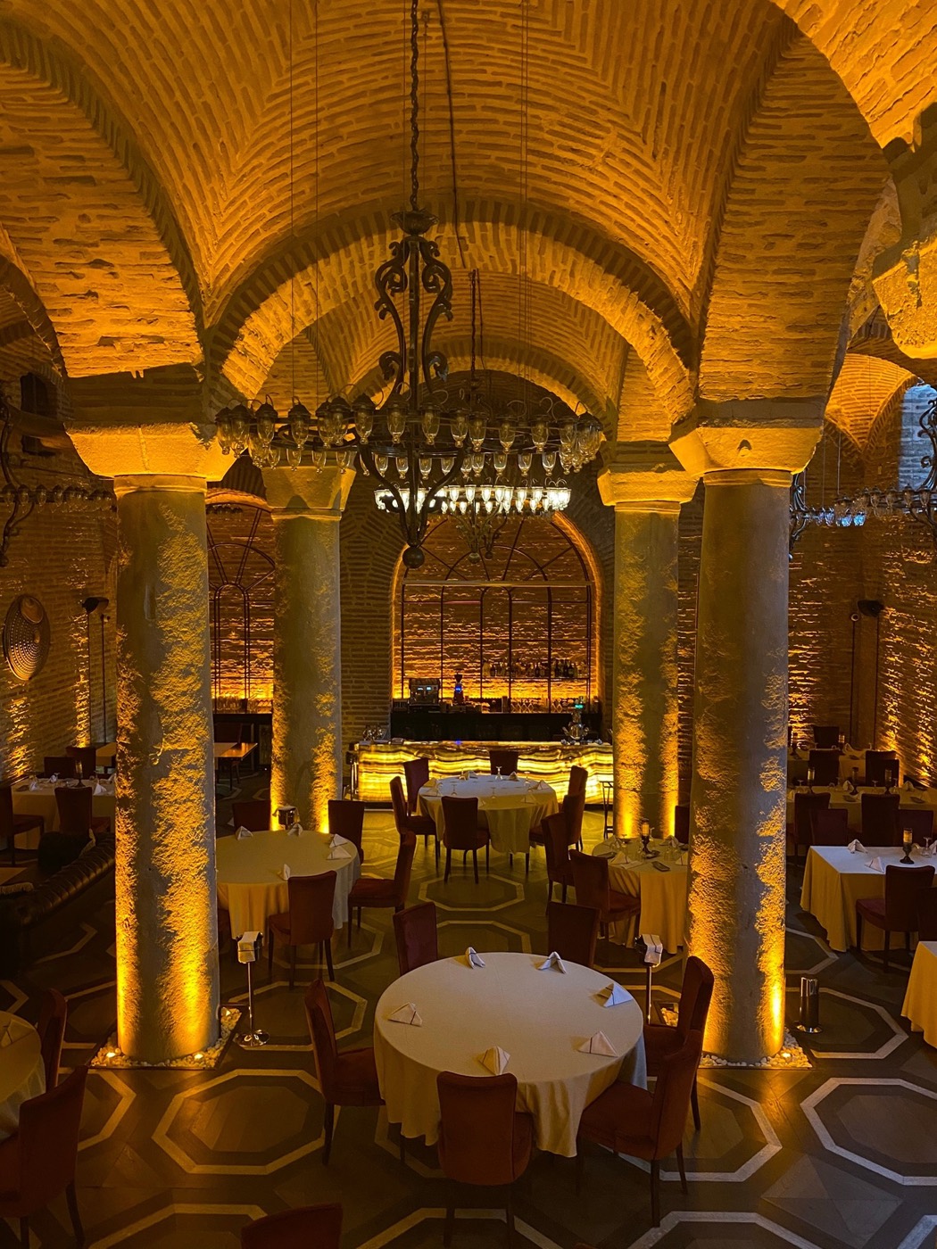 Salle à manger voûtée en pierre, arches éclairées de teintes dorées et lustre en cristal — ambiance de restaurant haut de gamme